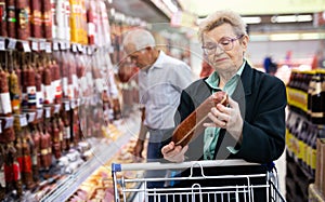 Mature woman with glasses picks out salami in the meat section of the supermarket