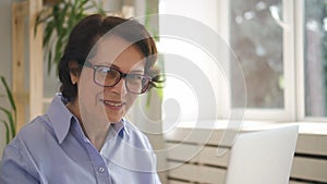 Mature woman in glasses working in cozy office on her laptop