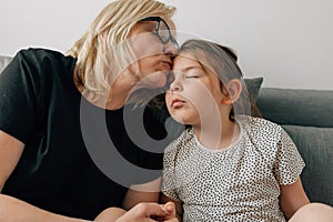 Mature woman grandmother kissing with love her granddaughter preschooler at home on sofa