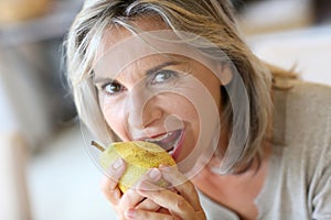 Mature woman with grey hair eating a pear