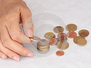 Mature, woman hand putting coins into a pile, heap, on white tablecloth background. Close. European euro coins, counting