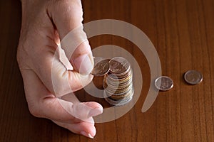 Mature woman hand putting coins into a pile on wooden table. Closeup. European euro coins, poverty concept. Counting photo