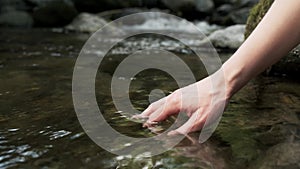 Mature woman hands touching and wetting the water of a lake in the mountain.