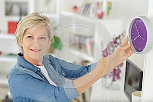 mature woman hanging clock on wall