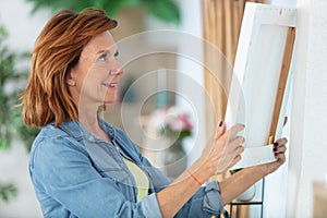 mature woman hanging picture on wall