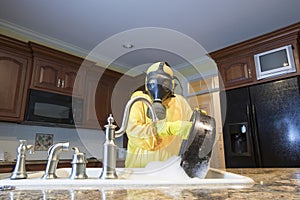 Mature woman in Haz Mat suit washing pot in kitchen sink photo