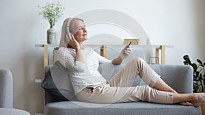 Mature woman in headphones enjoying favorite music, using phone