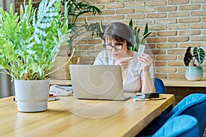 Mature woman in headphones having video chat with doctor, using laptop