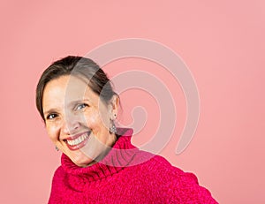 A mature woman in her early fifties with a pink turtleneck smiling at the camera with room for copy