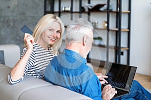 Mature woman holding debt card while man checking online account on netbook