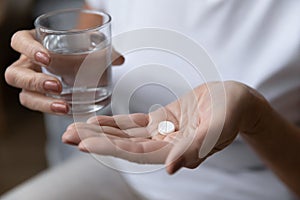 Mature woman holding glass of water and taking painkiller