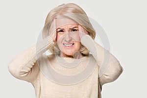 Mature woman holding head in hands feels unhealthy studio shot