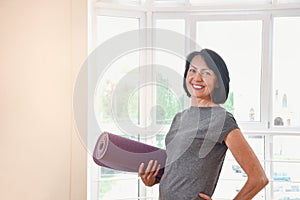 Mature woman holding rolled up exercise mat at gym