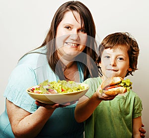 Mature woman holding salad and little cute boy with hamburger te