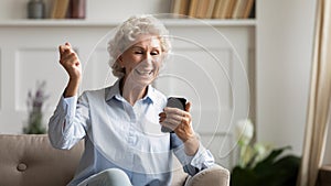 Mature woman holding smartphone feels excited by received great news