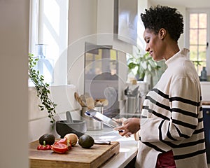 Mature Woman At Home In Kitchen With Ingredients Looking At Recipe On Digital Tablet