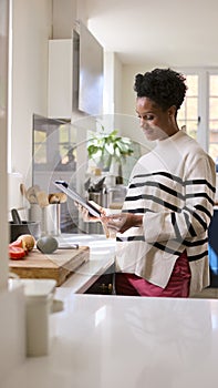 Mature Woman At Home In Kitchen With Ingredients Looking At Recipe On Digital Tablet