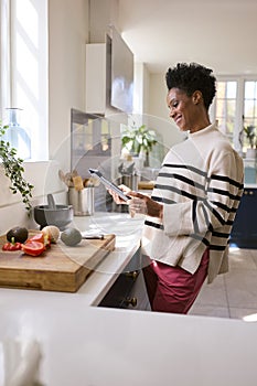 Mature Woman At Home In Kitchen With Ingredients Looking At Recipe On Digital Tablet