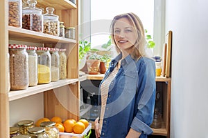 Mature woman at home in kitchen in pantry, portrait of housewife, female looking at camera