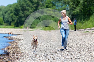 Mature woman jogs with a dog riverside