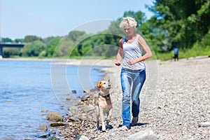 Mature woman jogs with a dog riverside