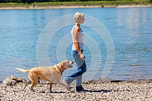 Mature woman jogs with a dog riverside