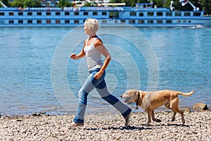 Mature woman jogs with a dog riverside