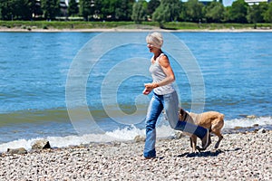 Mature woman jogs with a dog riverside