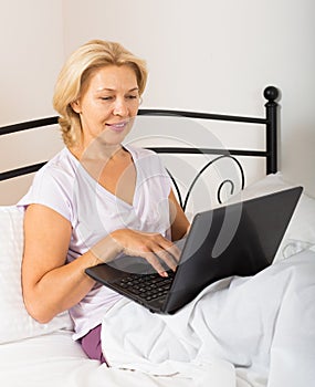 Mature woman with laptop in bed