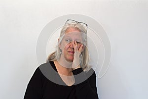 Mature woman with long white hair, hand rubbing eye, glasses raised, neutral background, copy space