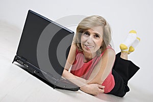 Mature woman lying on wooden floor using laptop