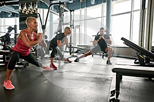 Mature woman and man doing side lunge exercise under trainer& x27;s supervision