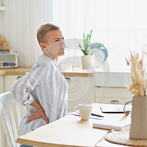 Mature woman massaging her back while working or studying on laptop online at home