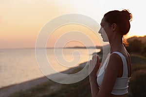 Mature woman meditating near sea in evening. Space for text