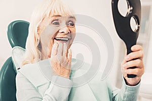 Mature woman with mirror looking at her denture photo