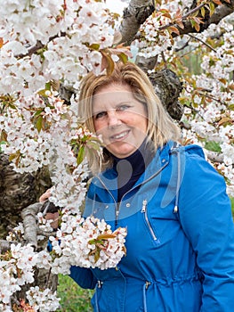 Mature woman  near to trees in landscape of fields with cherry trees in flowering season