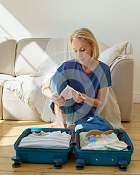 Mature woman packing her suitcase while preparing to travel during pandemic time
