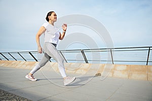 Mature woman performing morning jog on the city bridge. Active people and sport concept