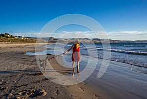 Mature woman and pet dog walking together on empty beach in the new normal after coronavirus