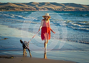 Mature woman and pet dog walking together on empty beach in the new normal after coronavirus