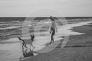 Mature woman and pet dog walking together on empty beach in the new normal after coronavirus