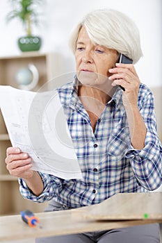 Mature woman on phone assembling furniture at new house