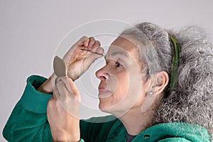 Mature woman plucking eyebrows on grey background