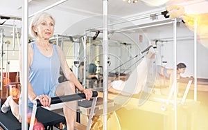 Mature woman practicing pilates stretching exercises on reformer at gym