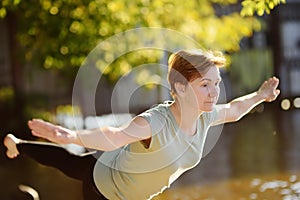 Mature woman practicing yoga outdoor exercise on the beach near the river.