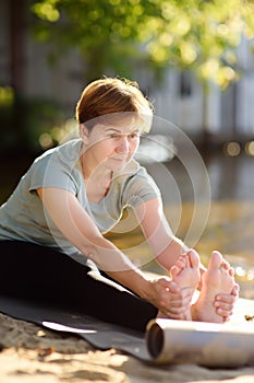 Mature woman practicing yoga outdoor exercise on the beach near the river