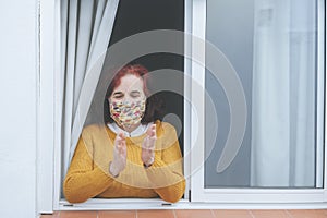 Mature woman with protective mask clapping at the window