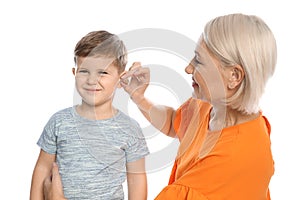 Mature woman putting hearing aid in little grandson`s ear