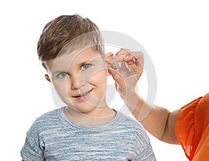 Mature woman putting hearing aid in little grandson`s ear on white background