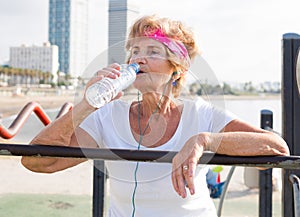 Mature woman quenches thirst from bottle after fitness session on beach